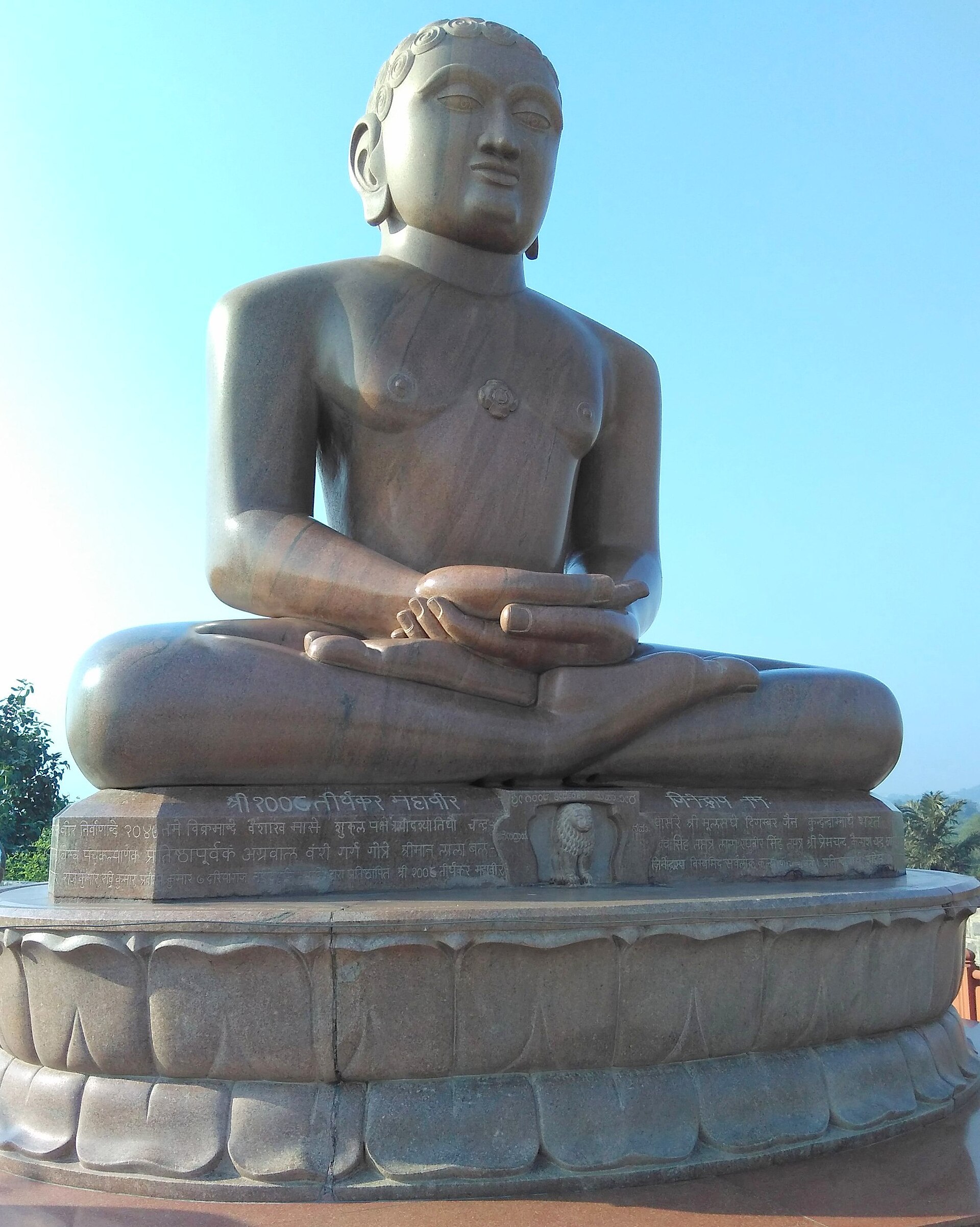 Granite statue of Bhagwan Mahaveer seated in padmasana against a clear sky at Ahinsa Sthal, Mehrauli