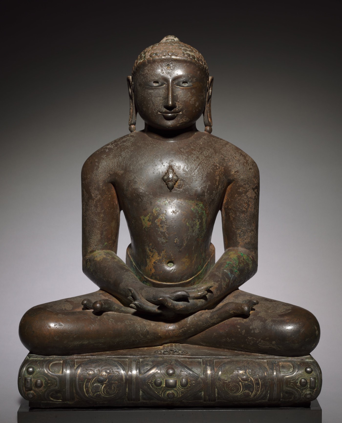 A bronze Jina seated in deep meditation, 10th–11th century, photographed against a dark ground